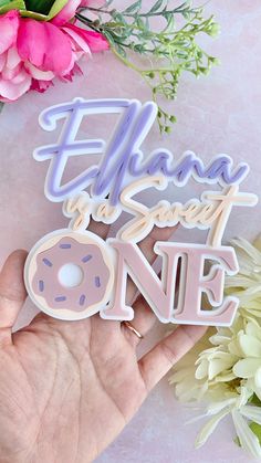 a hand holding a pink donut shaped sticker that says,'elana sweet one '