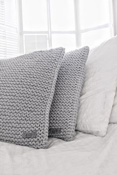 two gray pillows sitting on top of a bed next to each other in front of a window