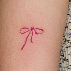 a woman's thigh with a red bow tattoo on her left side ribcage