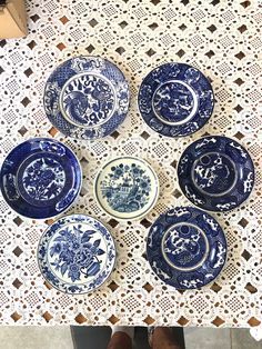 six blue and white plates sitting on top of a lace covered tablecloth next to a pair of brown shoes