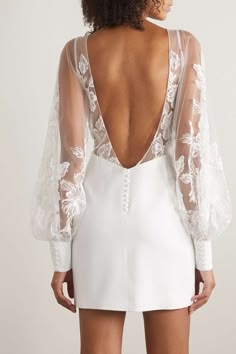 the back of a woman wearing a white dress with sheer sleeves and an open neckline