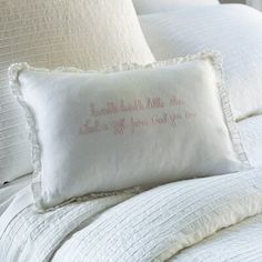 a bed with white sheets and pillows that have embroidered words on them, along with a pillow