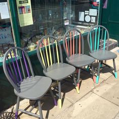 three chairs are sitting outside in front of a store window, painted with different colors