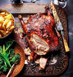 a roasting pan with meat, potatoes and broccoli next to it on a table