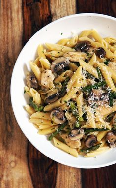 pasta with mushrooms, spinach and parmesan cheese in a white bowl on a wooden table