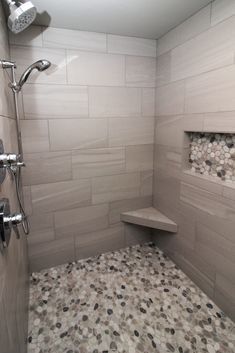 a walk in shower sitting next to a white tiled wall and floor with pebbles on it