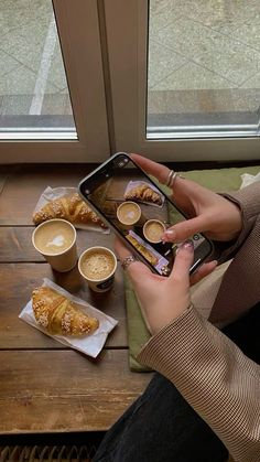 a woman sitting at a table with coffee and pastries on her lap, taking a photo