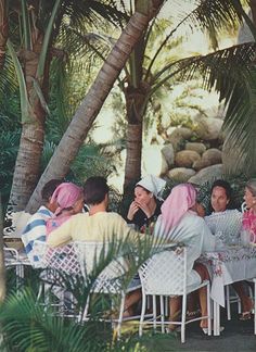 several people sitting at a table under palm trees