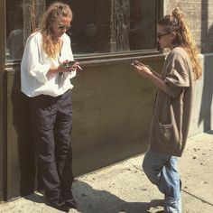 two women standing on the sidewalk looking at their cell phones