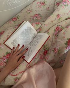 a woman laying in bed reading a book with her hand on top of the book