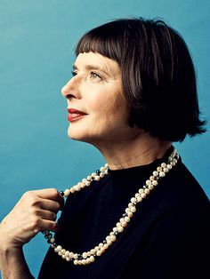 a woman with short hair wearing a black top and pearls necklace, looking up at the sky