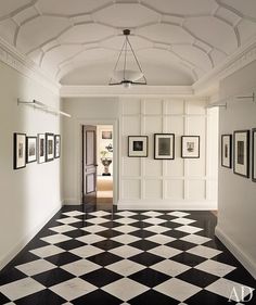 a hallway with black and white checkered flooring, framed pictures on the wall