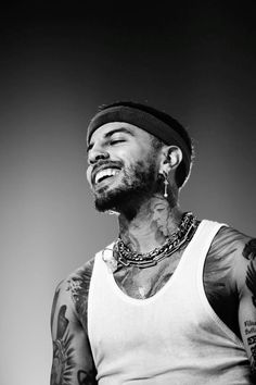 a black and white photo of a man with tattoos on his chest, wearing a tank top