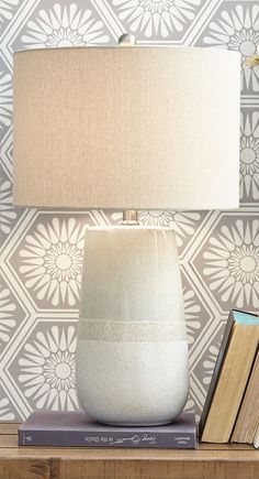 a table with a lamp and books on it next to a wallpapered wall