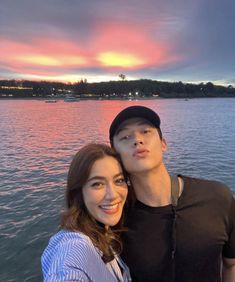 a man and woman standing next to each other in front of a body of water