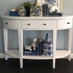 a white console table with books and vases on it's shelf in front of a blue wall