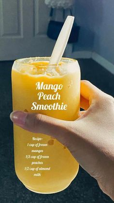 a hand holding a glass with mango peach smoothie