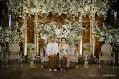 a man and woman sitting next to each other in front of a flower covered wall