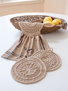 three pieces of crochet are sitting on a table next to a basket with lemons in it