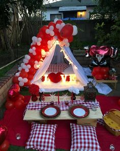 a table set up for a party with red and white balloons on the tent, plates and silverware