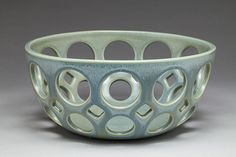 a blue bowl with circles and holes in the center on a gray background, sitting on top of a table