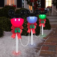 three mickey mouse heads with bows on top of snow covered ground in front of a house