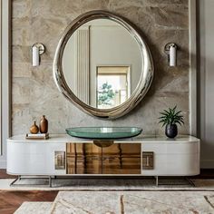 a round mirror on the wall above a white cabinet with a green glass top and gold accents