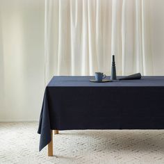 a table with a blue cloth and two cups on it, next to a white curtain