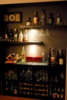 there is a shelf with bottles and glasses on it in the room that has many other liquors