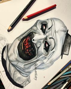 a drawing of a creepy clown with his mouth open and tongue out, surrounded by colored pencils