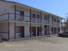 an empty parking lot in front of a two story building with red and white balconies