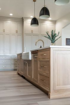 a large kitchen with white cabinets and wood flooring on the walls, along with two hanging lights