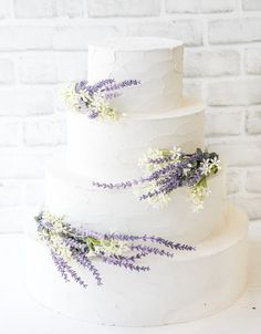 a three tiered white wedding cake with lavender flowers on the top and bottom layer