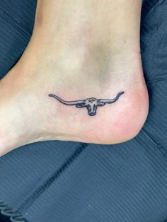 a small tattoo on the foot of a person with a longhorn bull skull in it