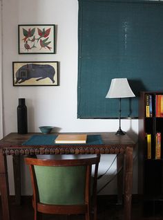 a desk with a lamp, books and pictures on the wall above it in a living room