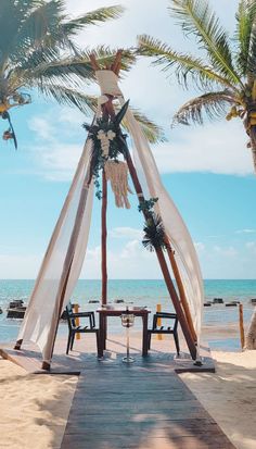 a gazebo set up on the beach for an outdoor ceremony with palm trees in the background