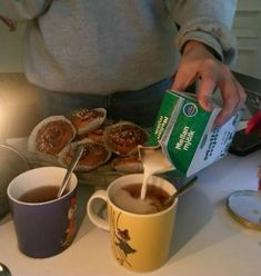 a person pouring coffee into two mugs with pastries on the table next to them