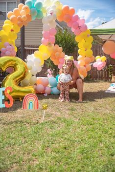 a woman and her child are sitting in front of balloons that spell out the number two