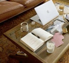 a coffee table with an open book, candle and apple laptop sitting on top of it