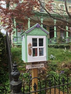 a little green house sitting on top of a wooden post in front of a fence