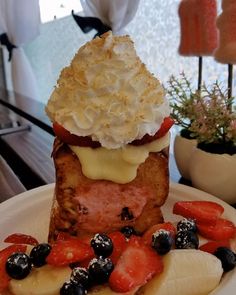 a white plate topped with french toast and fruit covered in whipped cream next to a potted plant