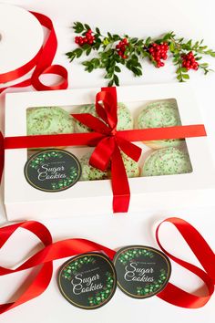 two cookies wrapped in red ribbon and decorated with green sprinkles on top of a white box