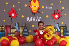 a little boy sitting on the floor with balloons in front of him and an iron man balloon