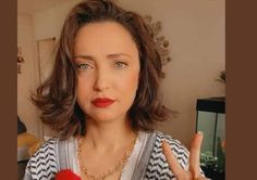 a woman is making the peace sign with her hand and holding a red object in front of her face