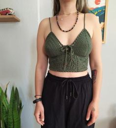 a woman standing in front of a plant wearing black pants and a green crop top