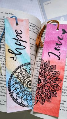 two bookmarks with the words love and peace on them sitting next to an open book