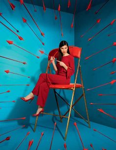 a woman sitting in a red chair with arrows on the wall behind her and one leg up