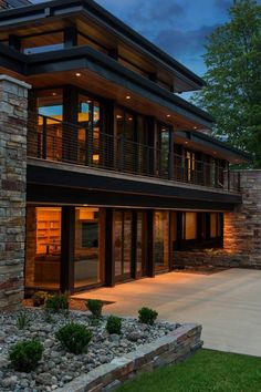 a modern house is lit up at night with lights on the windows and stone walls