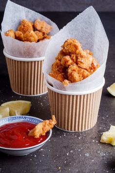 two paper cups filled with fried food next to ketchup and lemon wedges