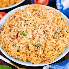 two plates of pasta with tomatoes and parmesan cheese on the side, next to silverware